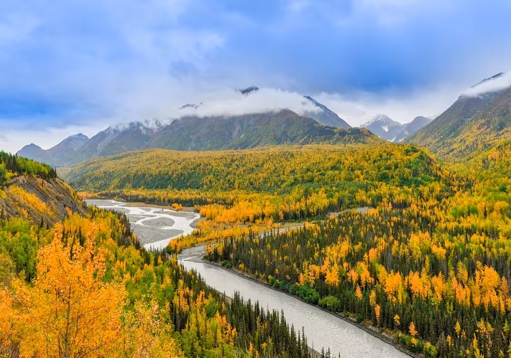 Breathtaking view of Alaska in autumn, with a river snaking through a valley ablaze with fall colors, illustrating the beauty of September travel.