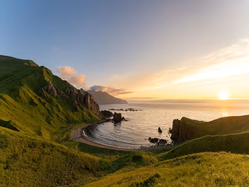 Vibrant green hillsides sloping to a picturesque beach cove in Alaska during summer, highlighting the beauty of coastal exploration.